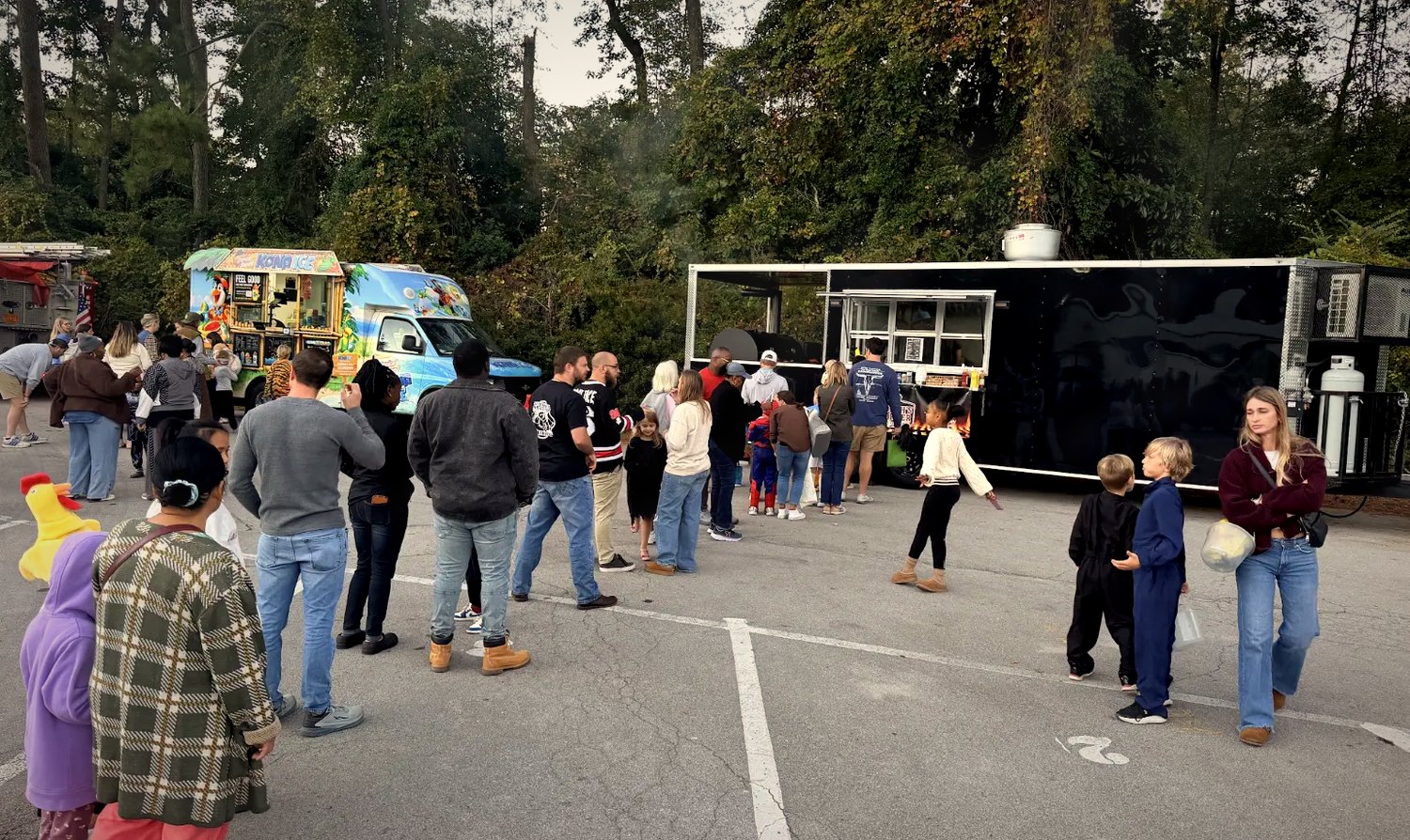 A long line of families and kids in costume waiting at the Coach's Corner food trailer at a community event
